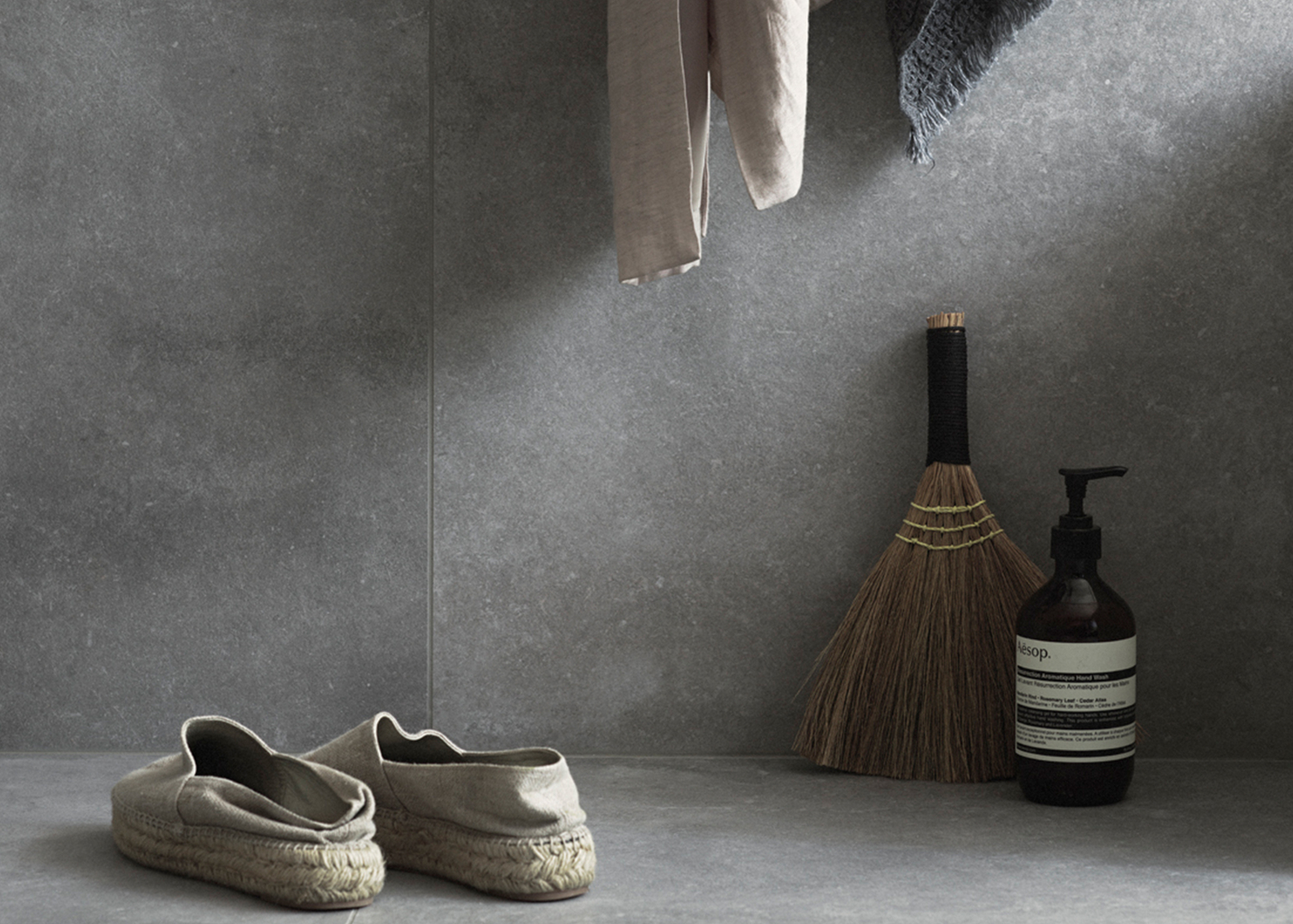 Miljöbild på grå granitkeramik i ett badrum. Tofflor och detaljer.